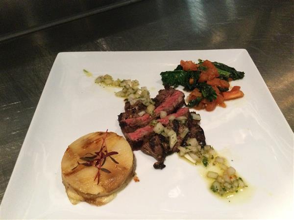 Entree of Grilled Skirt Steak with layered potato cake, braised collard greens, and chimichurri